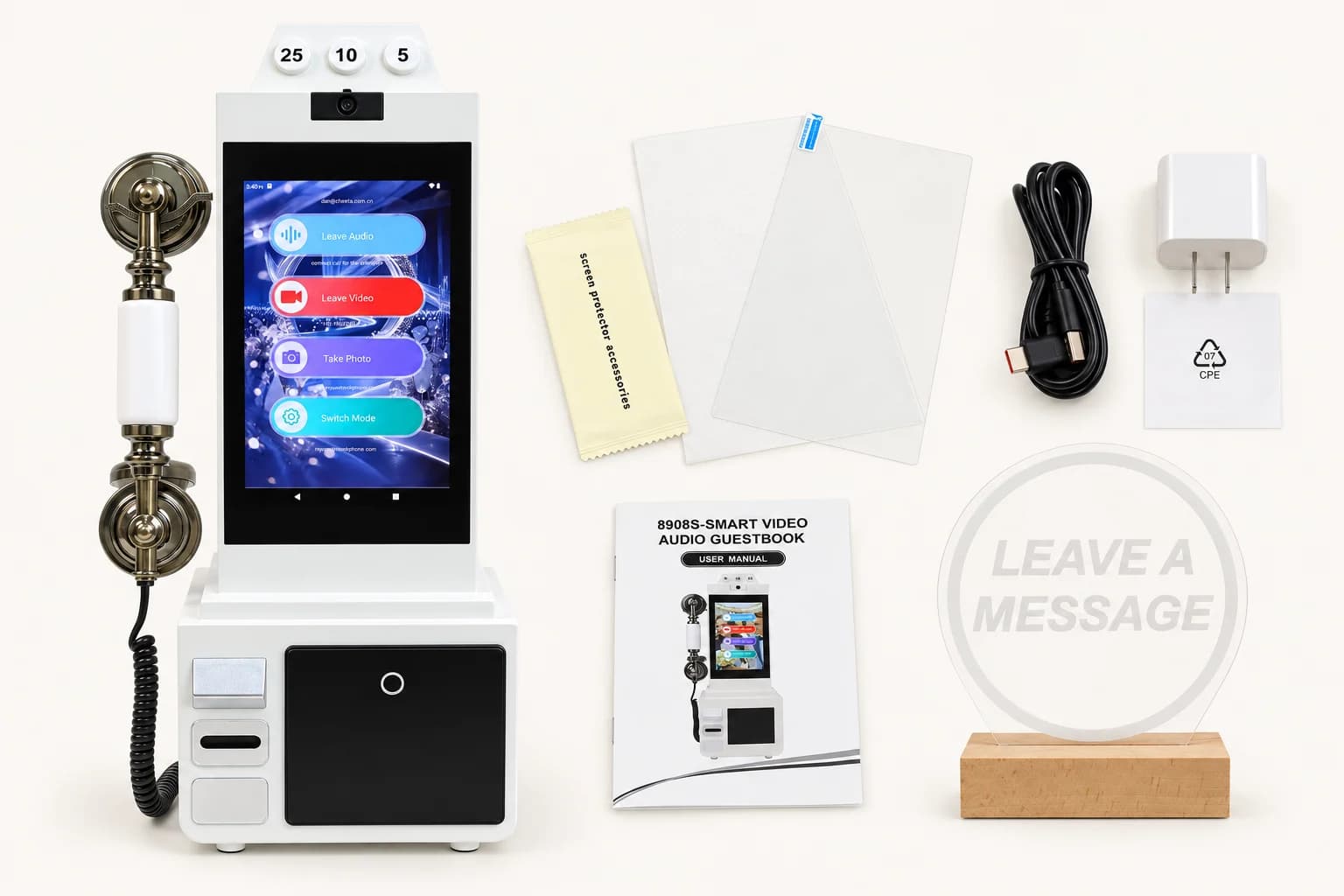 White video guestbook phone with its screen protector, black charging cable, white power adapter, printed user manual and round acrylic light sign on a wooden base.